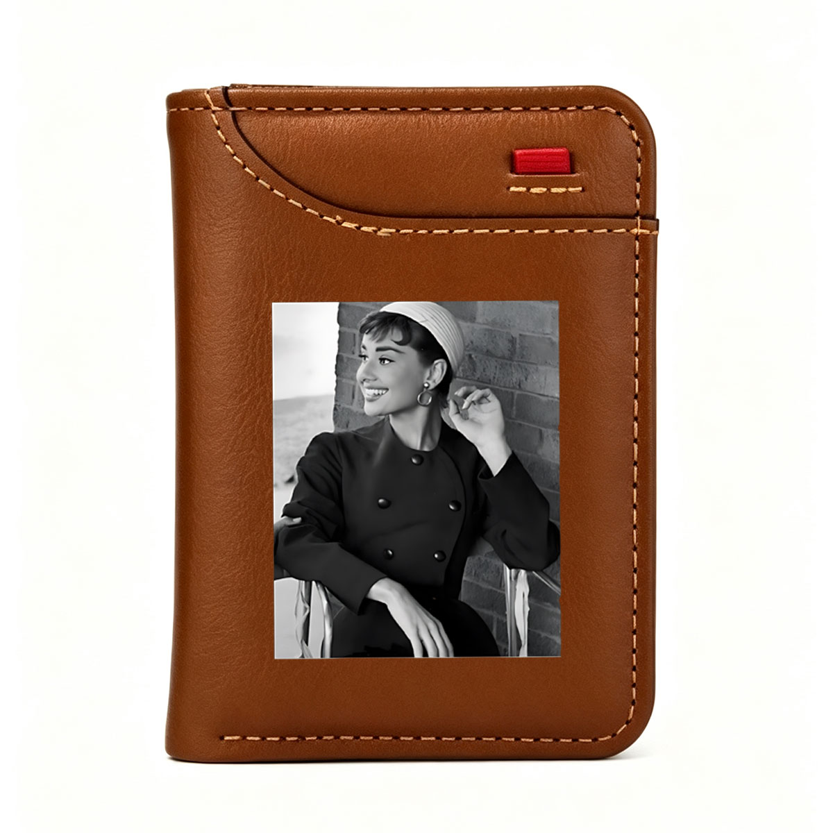 Audrey Hepburn in a classic black coat and white hat, smiling elegantly against a brick wall. - Vertical Style Wallet