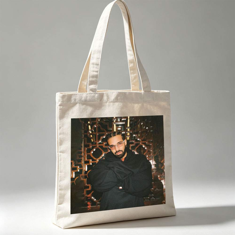 Drake in a Stylish Pose Against an Ornate Background Wearing Glasses and a Black Hoodie - Canvas tote bags