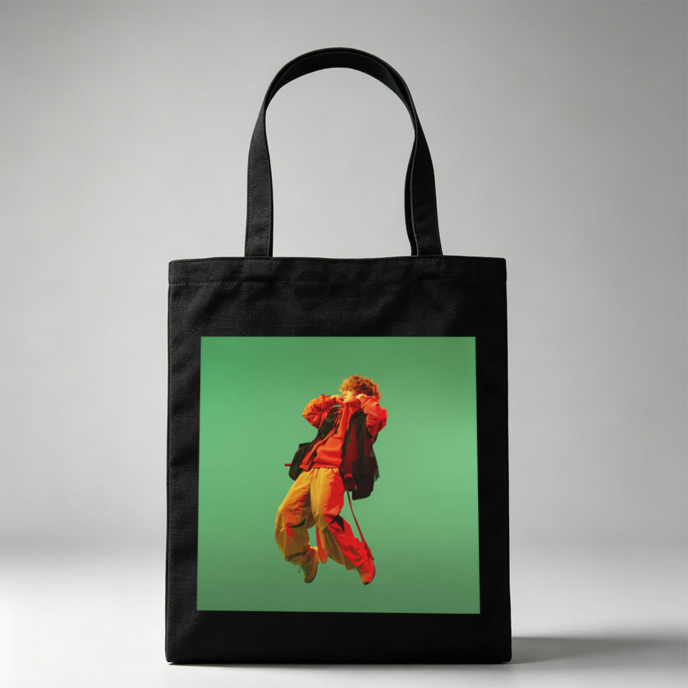 Troye Sivan in a vibrant red and yellow outfit mid-jump against a green background - Canvas tote bags