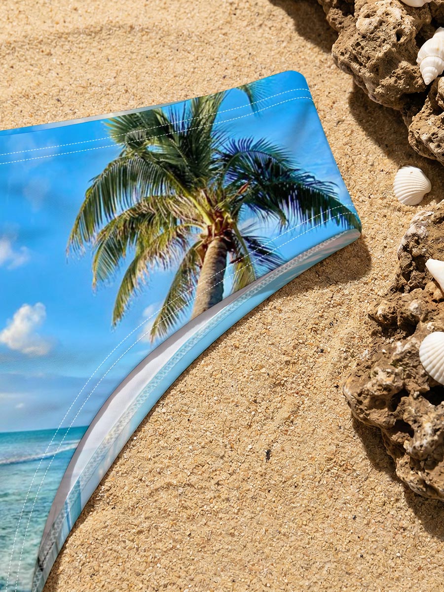 Tropical beach with palm tree leaning over clear blue water under a bright sky. -  Men's swim trunks