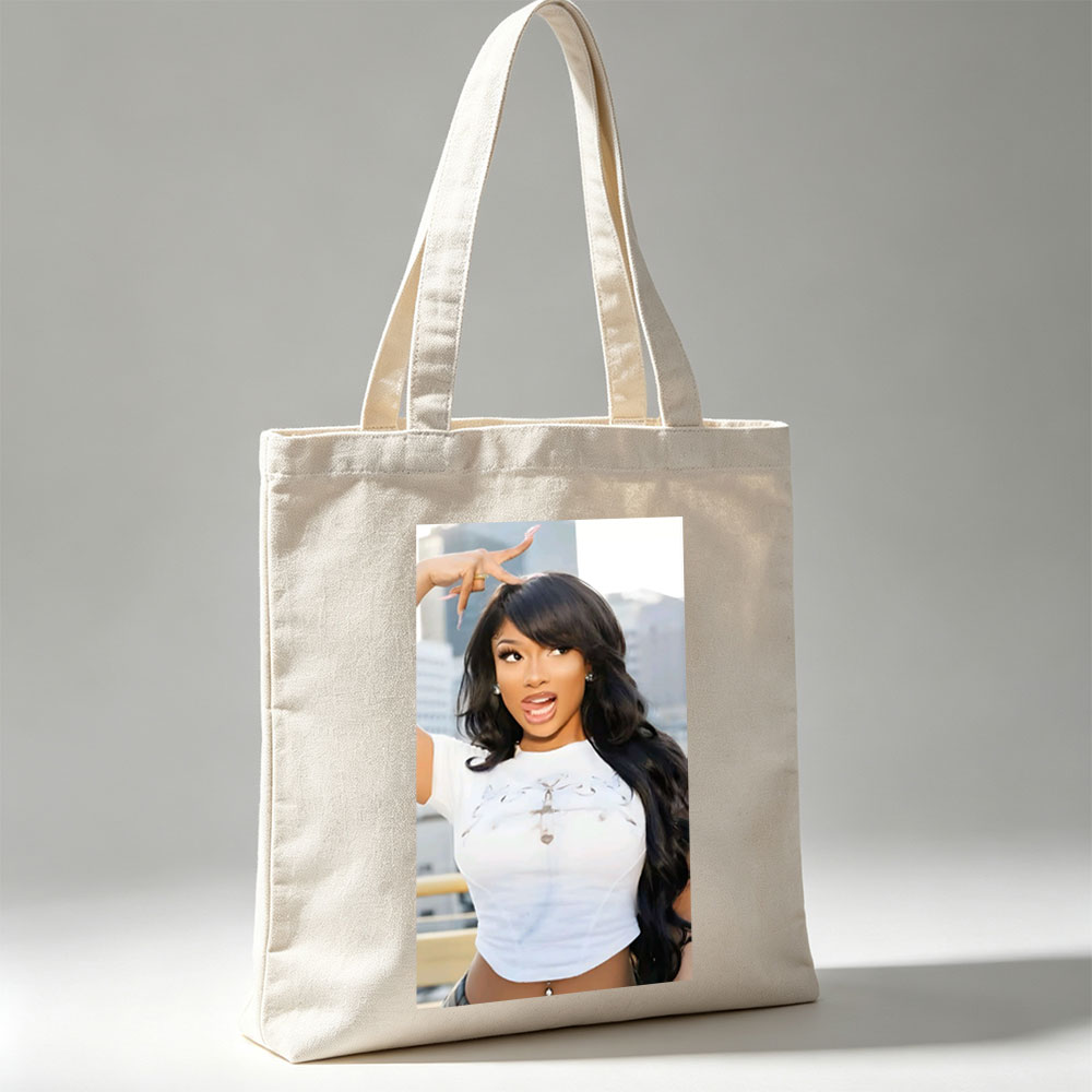 Megan Thee Stallion in a Bold Pose Wearing a White Crop Top with Cross Design and Long Black Hair Against a City Skyline Background - Canvas tote bags