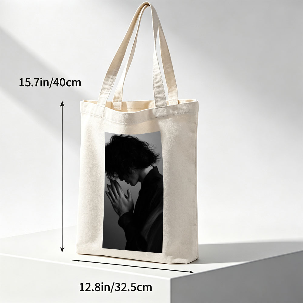 Yojiro Noda in a contemplative pose with hands clasped, captured in dramatic black and white lighting. - Canvas tote bags