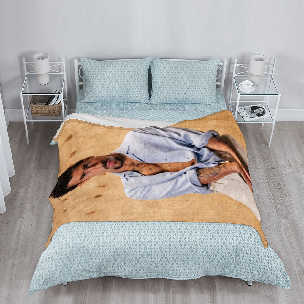Bad Bunny in a Casual Pose Wearing an Open Light Blue Shirt and Beige Pants Against a Wooden Background - Blankets