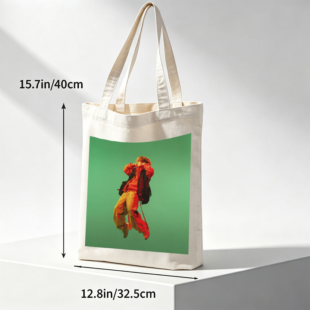 Troye Sivan in a vibrant red and yellow outfit mid-jump against a green background - Canvas tote bags