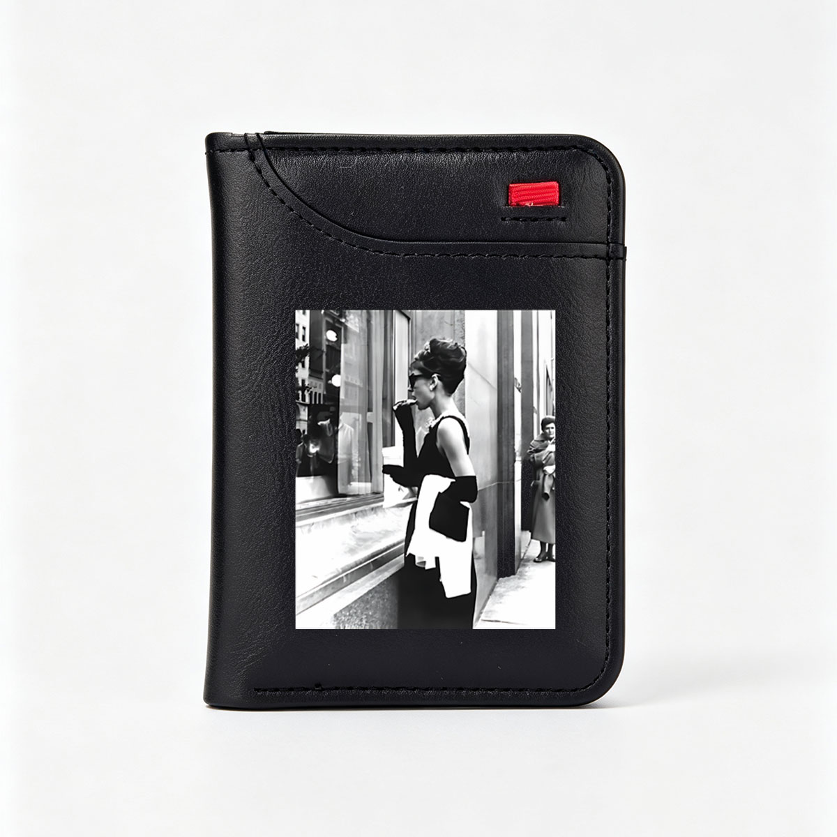 Audrey Hepburn in iconic black dress and sunglasses, standing by a window display, holding a white scarf and cigarette holder. - Vertical Style Wallet