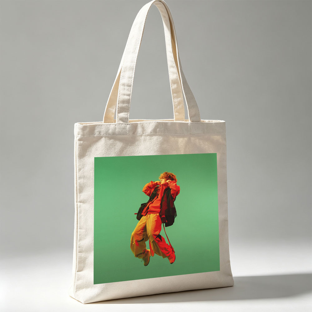 Troye Sivan in a vibrant red and yellow outfit mid-jump against a green background - Canvas tote bags