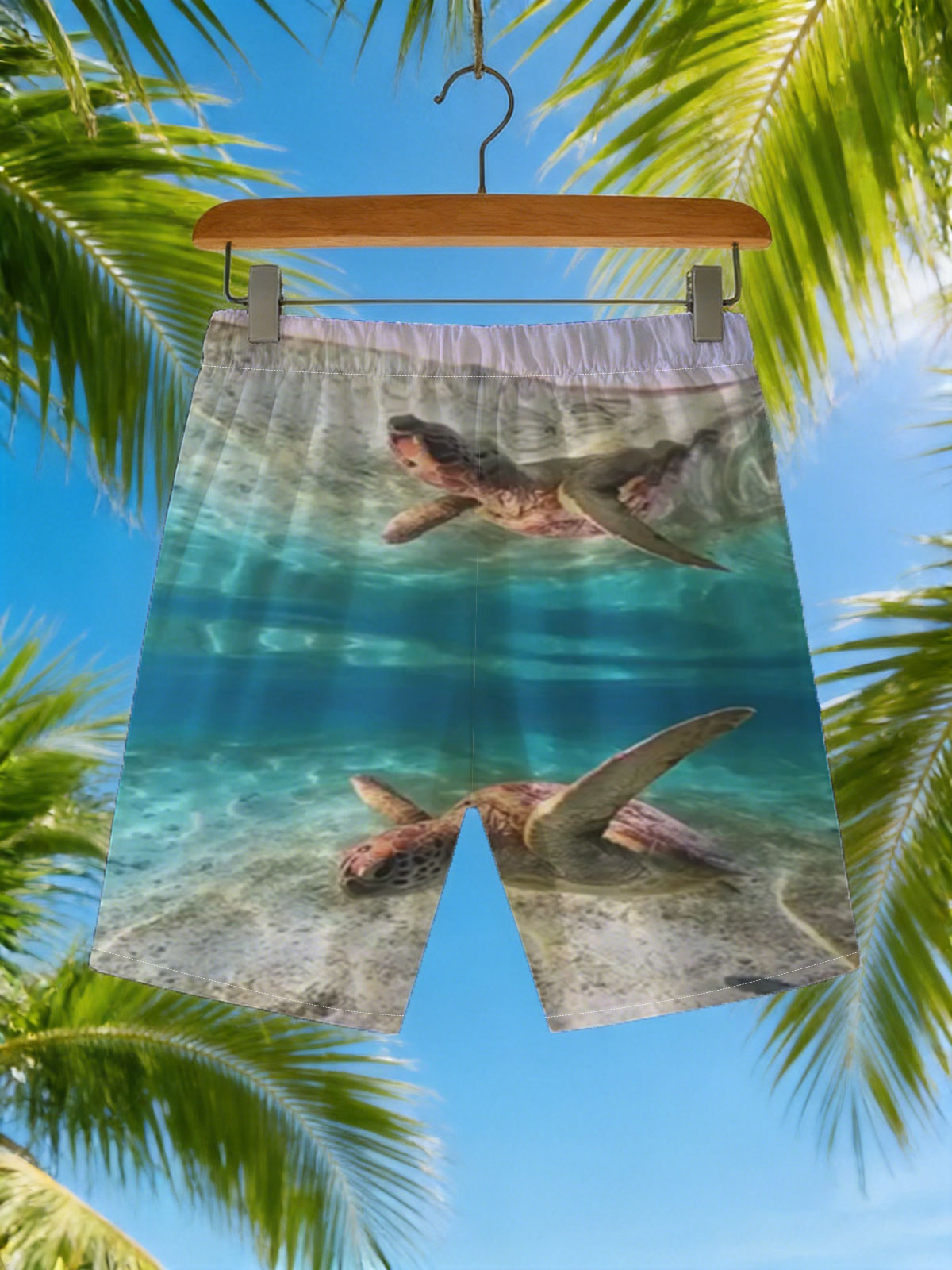Sea turtles swim gracefully in clear blue waters, one near the surface and one gliding over sandy ocean floor. -  Beach shorts