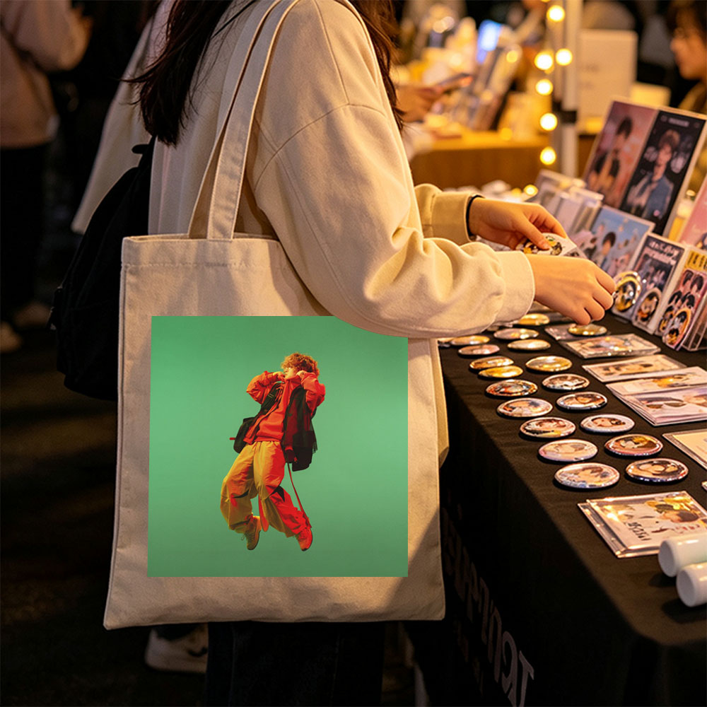 Troye Sivan in a vibrant red and yellow outfit mid-jump against a green background - Canvas tote bags