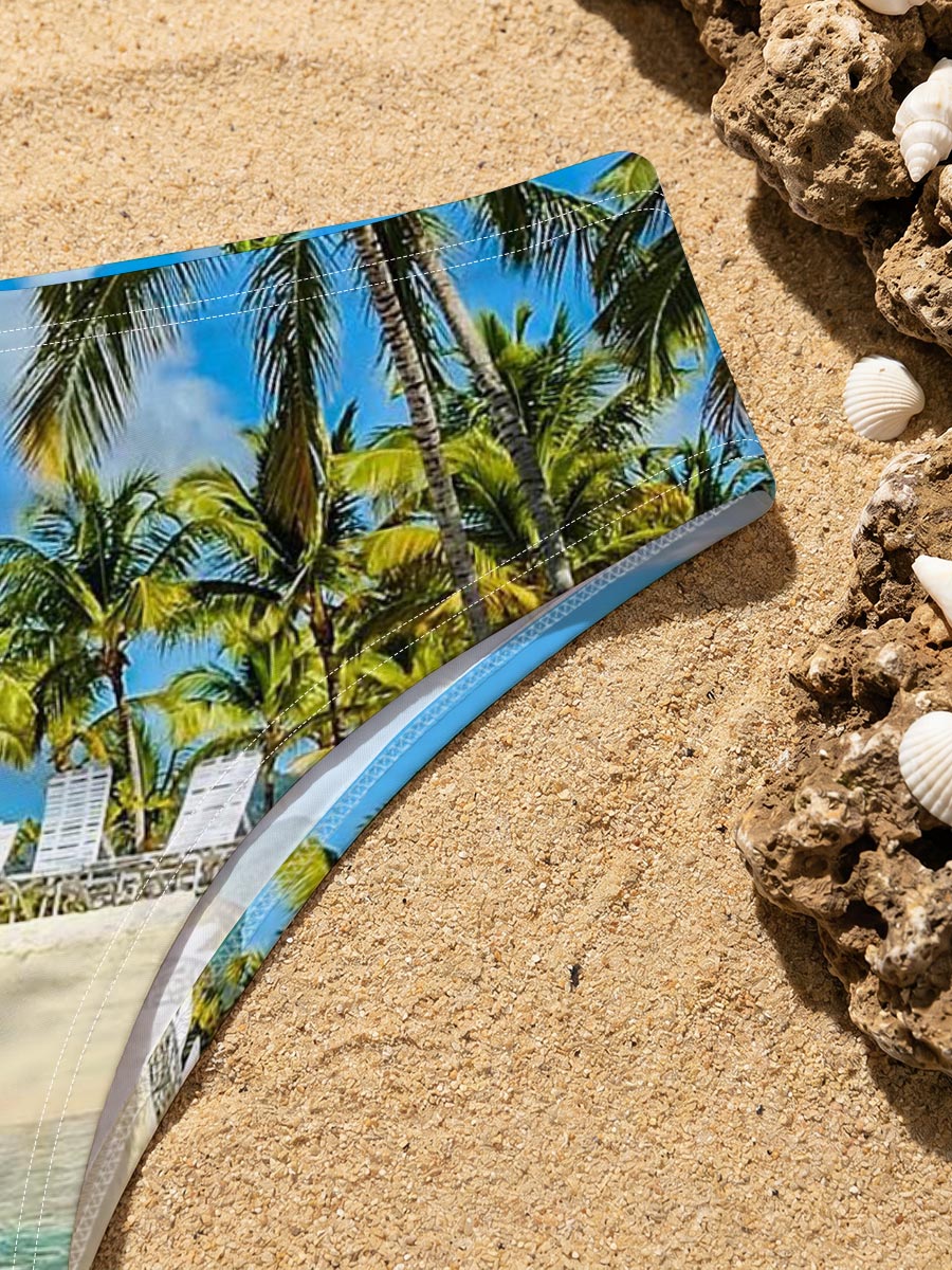 Crystal clear waters meet sandy beach with palm trees and lounge chairs under a bright blue sky. -  Men's swim trunks