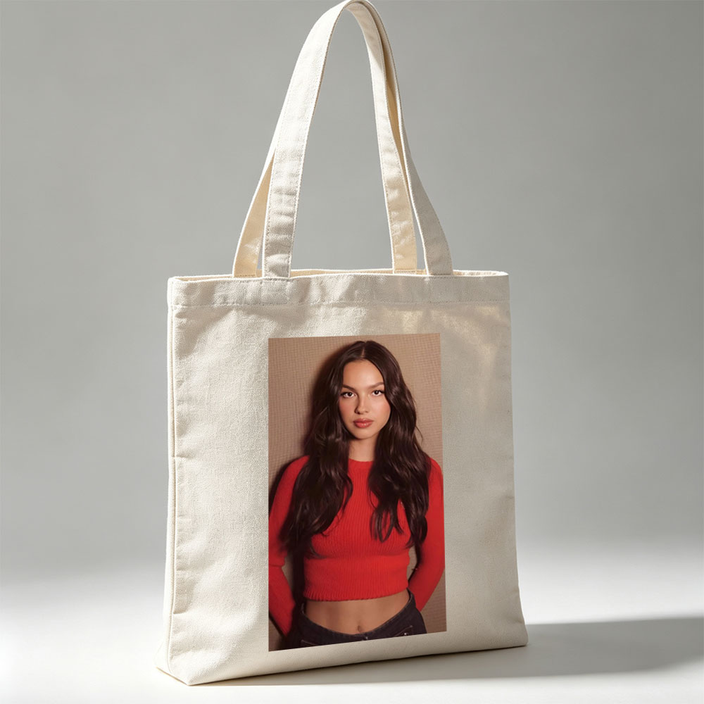 Olivia Rodrigo in a Bold Red Crop Top and Jeans, Striking a Confident Pose Against a Textured Background - Canvas tote bags