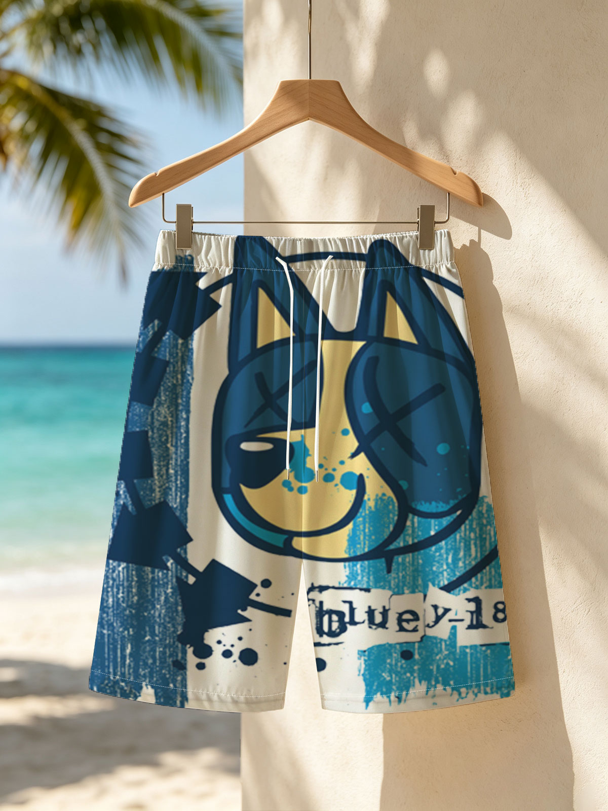 Bluey-182: A stylized blue and yellow cat face with X eyes, arrows, and splatter effects on a textured blue background. -  Beach shorts