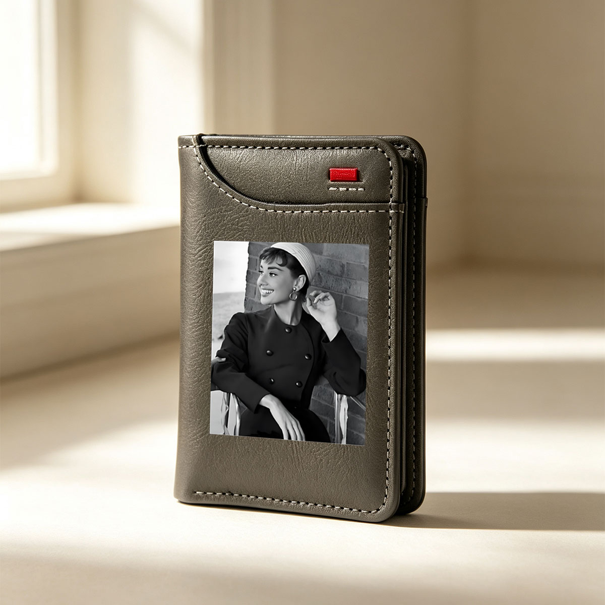 Audrey Hepburn in a classic black coat and white hat, smiling elegantly against a brick wall. - Vertical Style Wallet