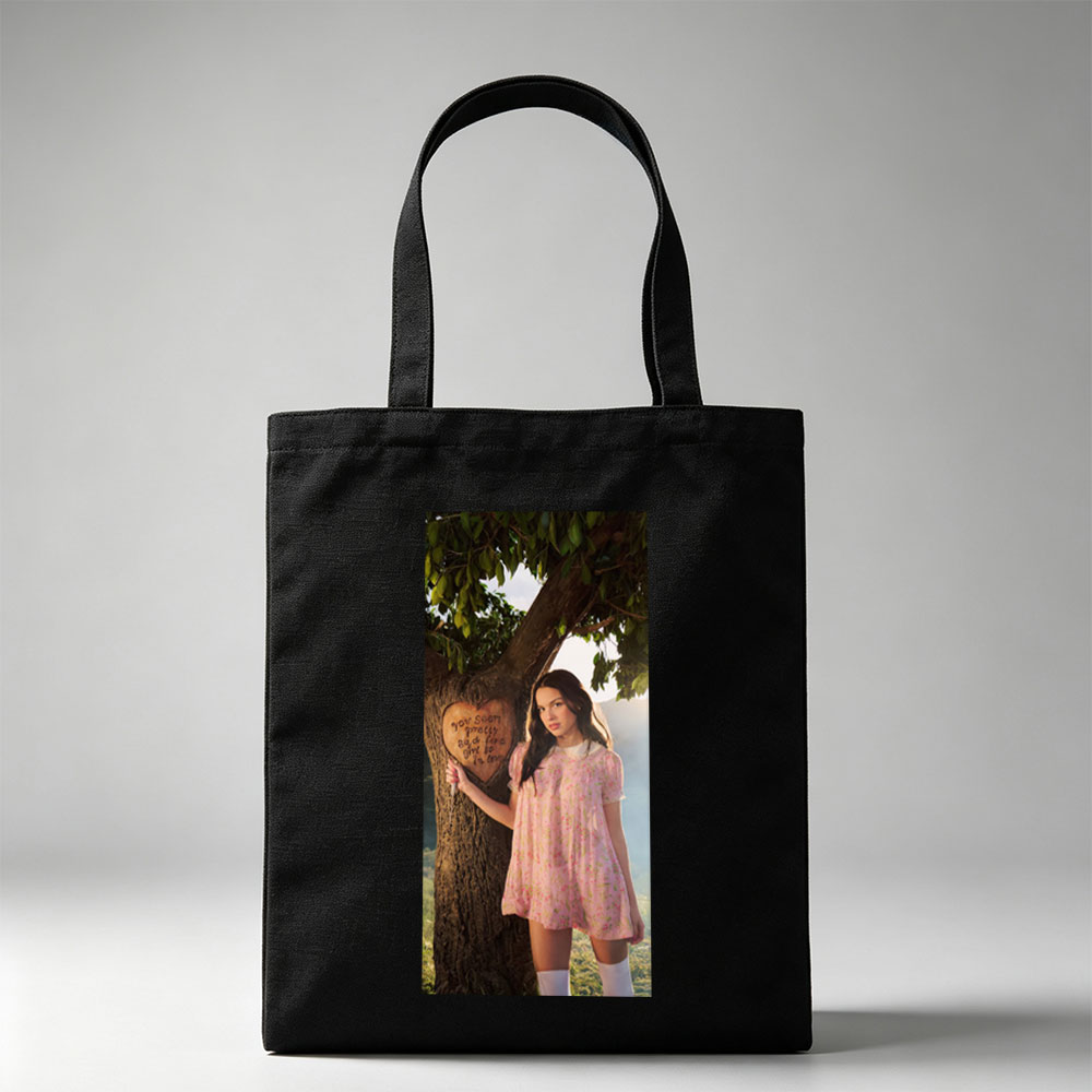 Olivia Rodrigo in a Romantic Outdoor Scene Wearing a Pink Floral Dress Leaning Against a Tree with a Heart Carved Message - Canvas tote bags