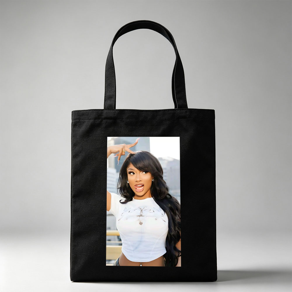 Megan Thee Stallion in a Bold Pose Wearing a White Crop Top with Cross Design and Long Black Hair Against a City Skyline Background - Canvas tote bags