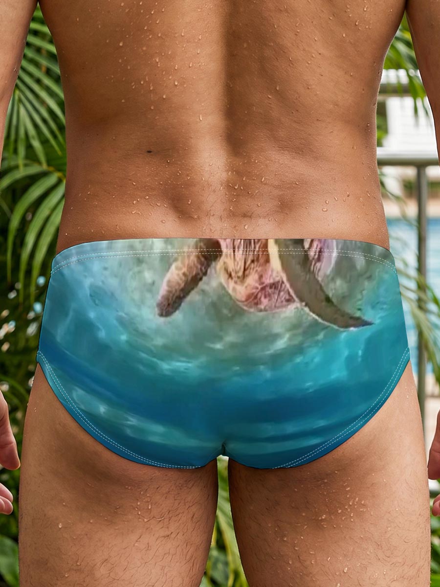 Sea turtles swim gracefully in clear blue waters, one near the surface and one gliding over sandy ocean floor. -  Men's swim trunks