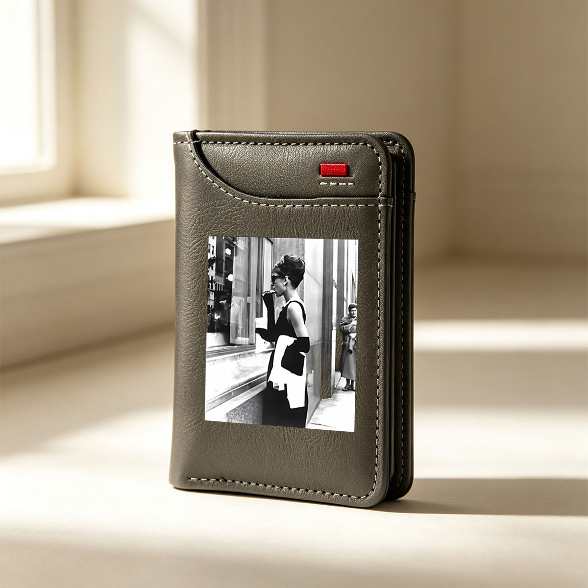 Audrey Hepburn in iconic black dress and sunglasses, standing by a window display, holding a white scarf and cigarette holder. - Vertical Style Wallet