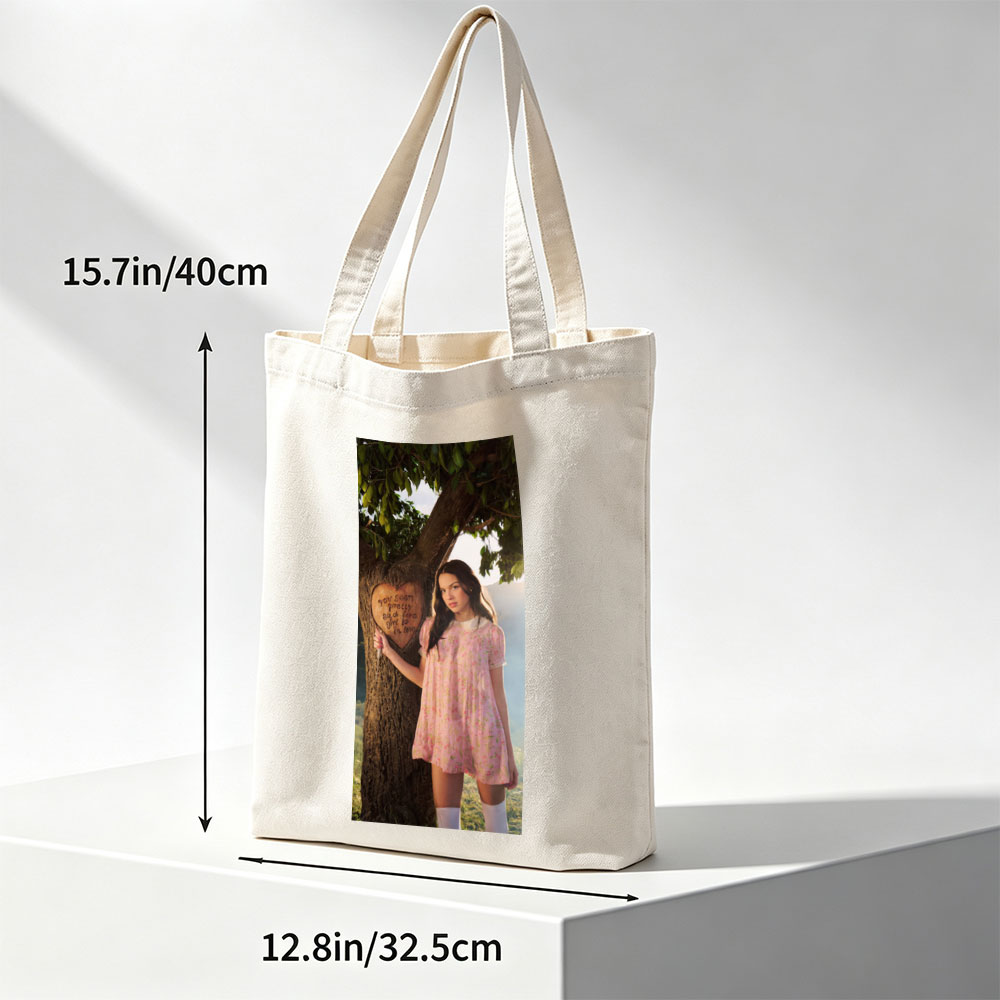 Olivia Rodrigo in a Romantic Outdoor Scene Wearing a Pink Floral Dress Leaning Against a Tree with a Heart Carved Message - Canvas tote bags