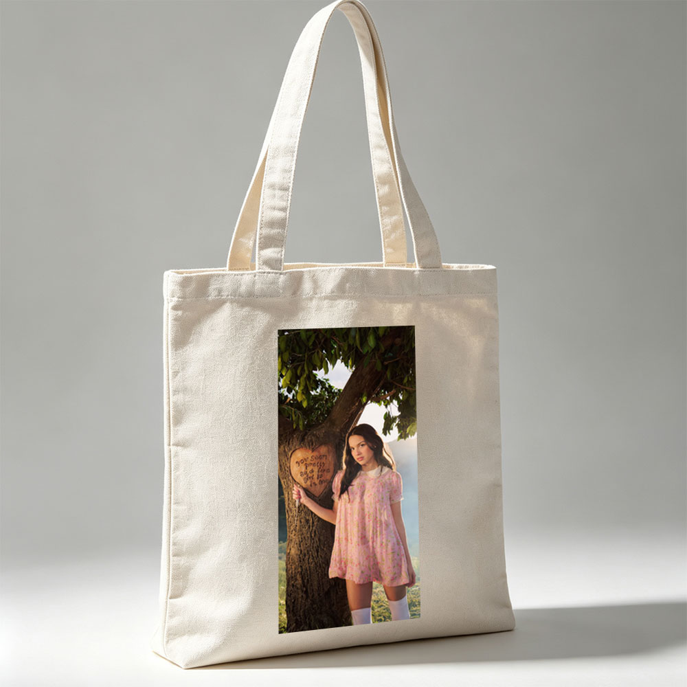 Olivia Rodrigo in a Romantic Outdoor Scene Wearing a Pink Floral Dress Leaning Against a Tree with a Heart Carved Message - Canvas tote bags
