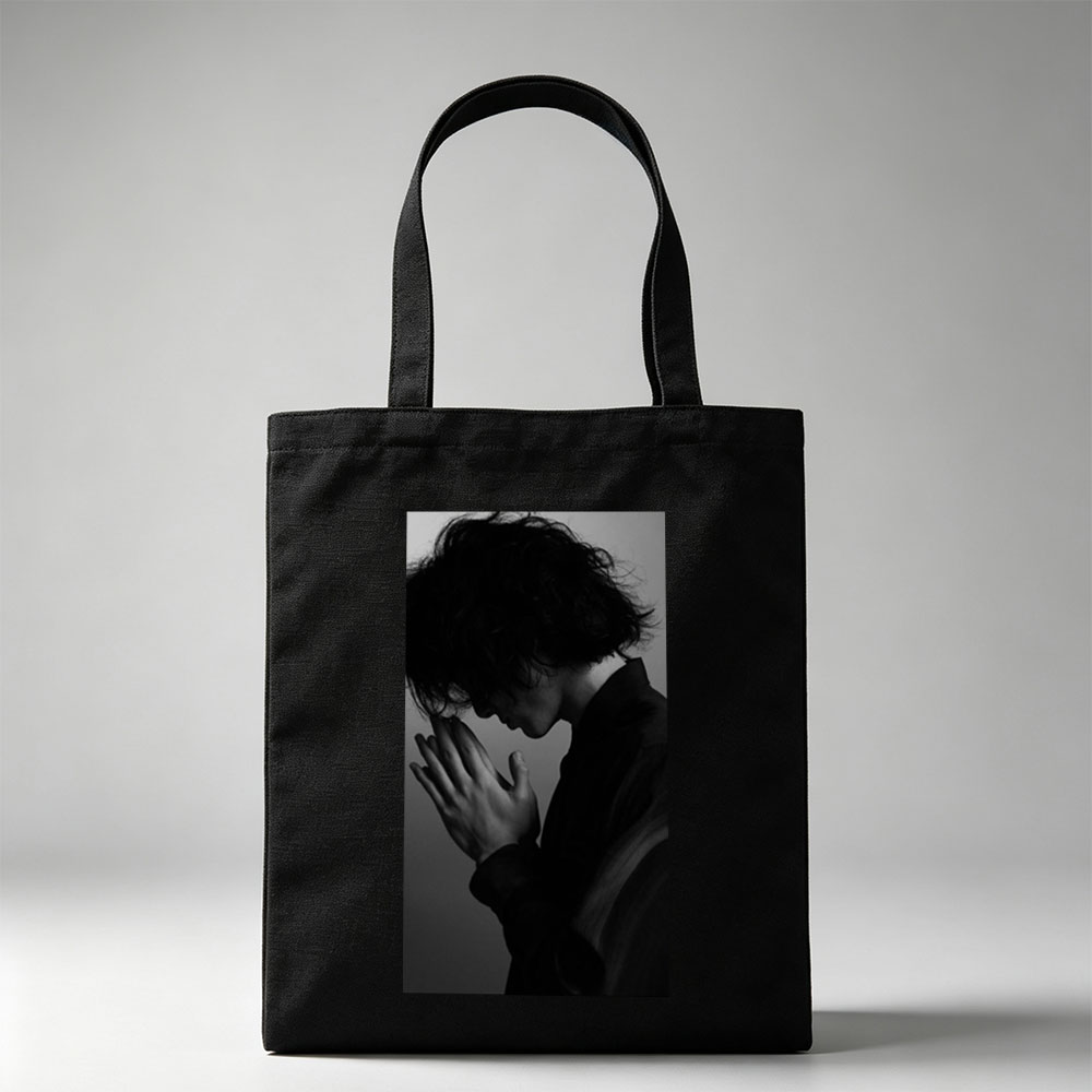Yojiro Noda in a contemplative pose with hands clasped, captured in dramatic black and white lighting. - Canvas tote bags
